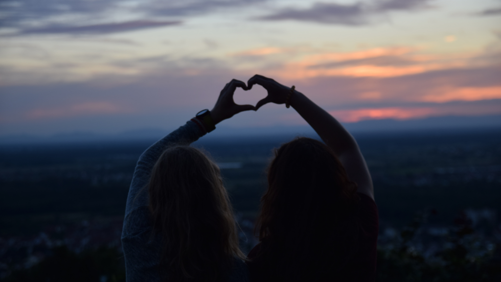 Two girls standing at a high place overlooking the city with their hands held up together to make a heart