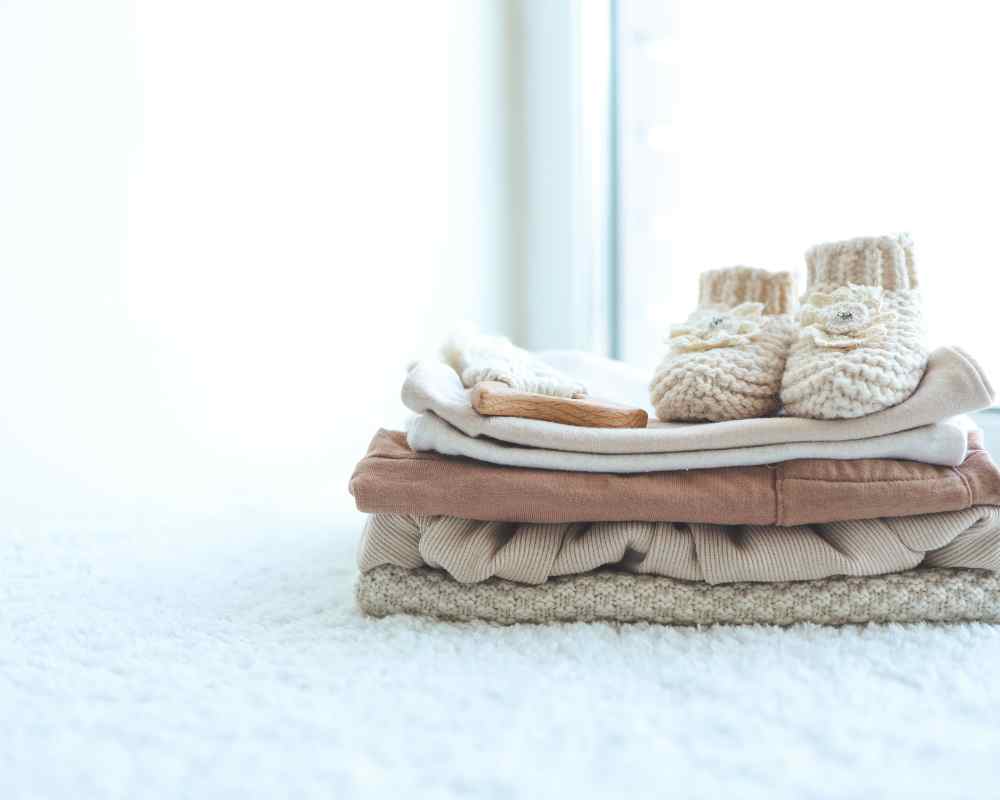 A pile of pink folded baby clothes with little white shoes on top