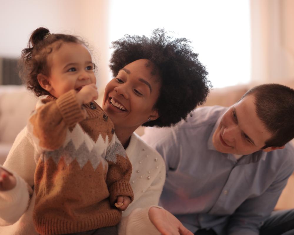 A woman and man sitting on the floor smiling with a toddler