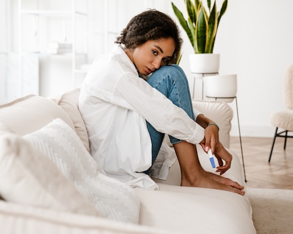 Girl sitting curled up on white sofa holding a pregnancy test